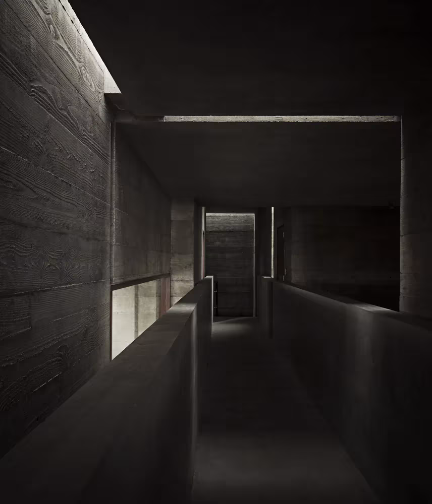 Pasillo en penumbra de hormigón encofrado con luz cenital en la Casa Phoenix de Sebastián Mariscal Studio
