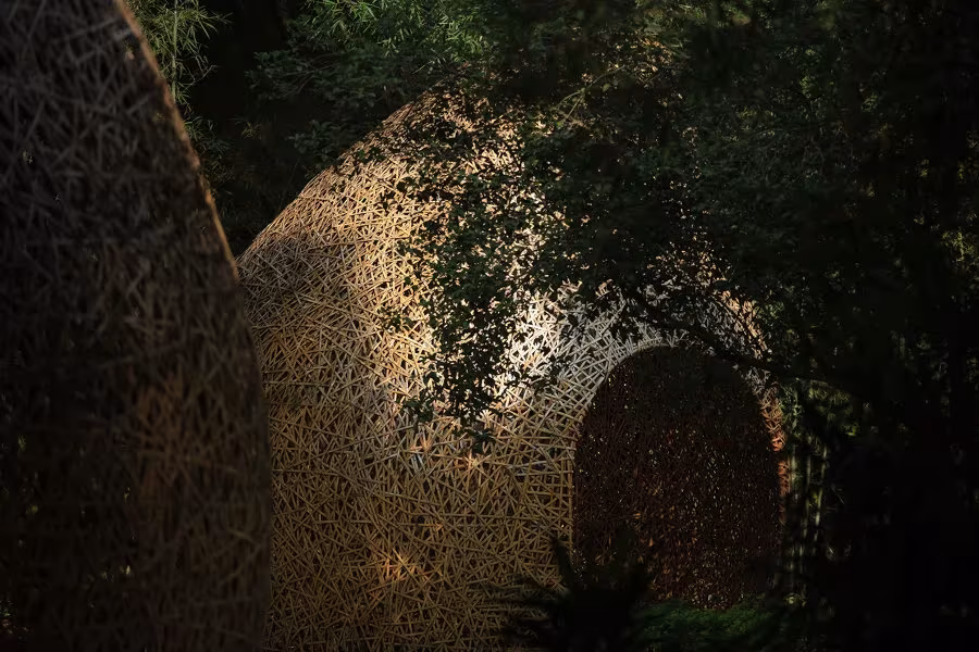 Cúpula de bambú trenzado con un hueco oscuro de entrada entre la vegetación, obra de LLLab. en Yangshuo