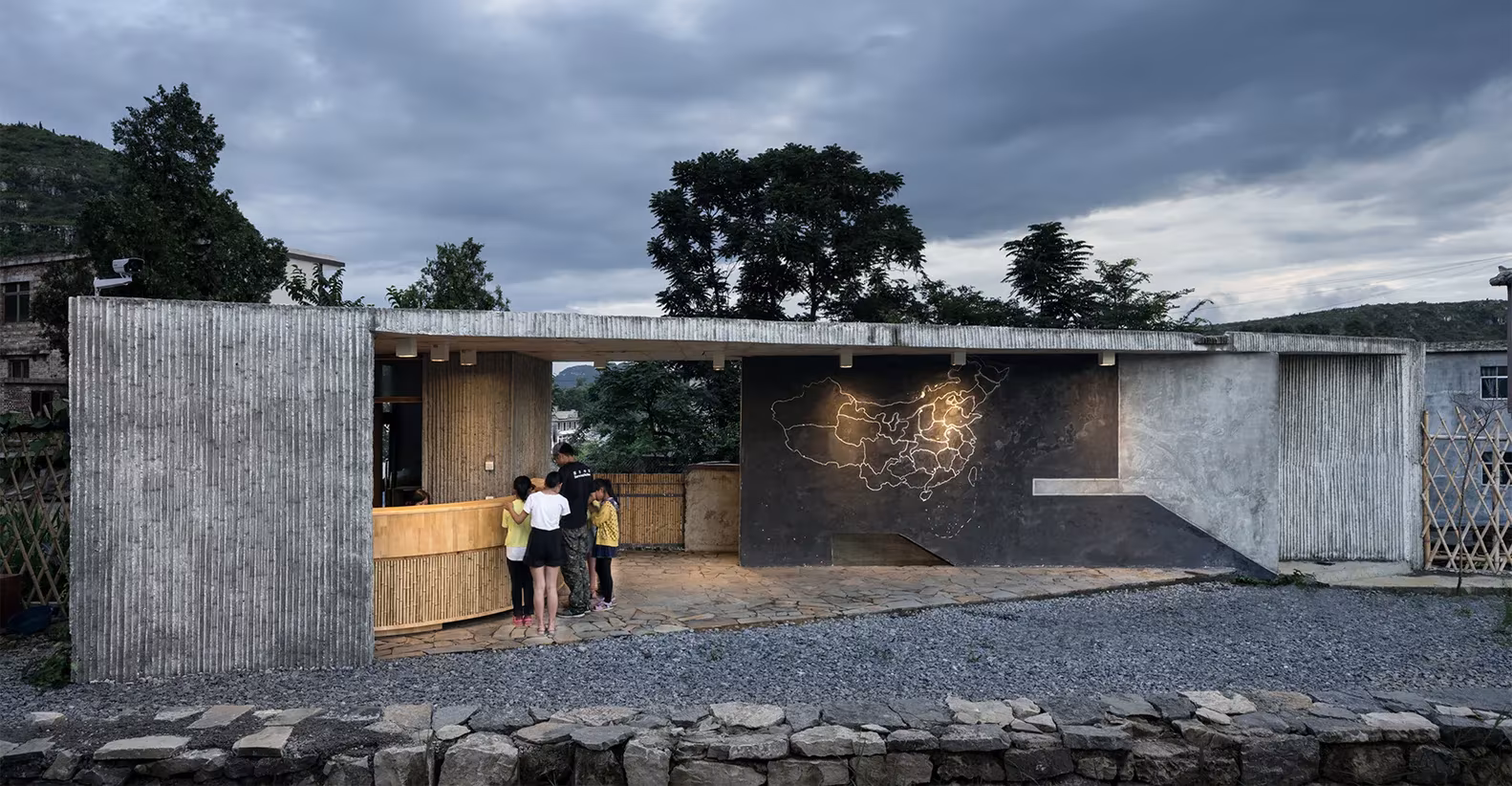 Edificio de hormigón y bambú con un muro de piedra al fondo junto al campamento de Pingqiao
