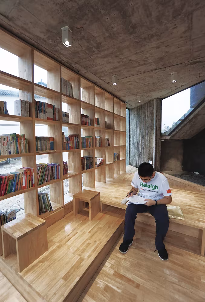 Biblioteca de estanterías de madera bajo techo de hormigón, con un joven leyendo, en el campamento de Pingqiao