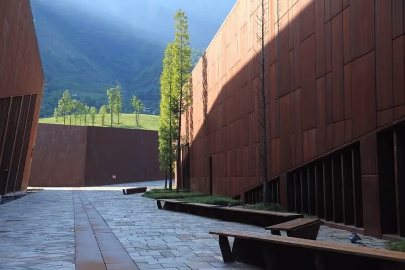 Patio de piedra con bancos entre muros de acero corten del Museo del Terremoto de Wenchuan