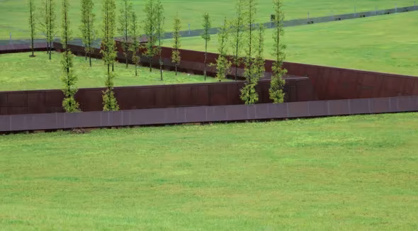 Franja de acero corten y hilera de árboles recién plantados sobre el césped del Museo de Wenchuan