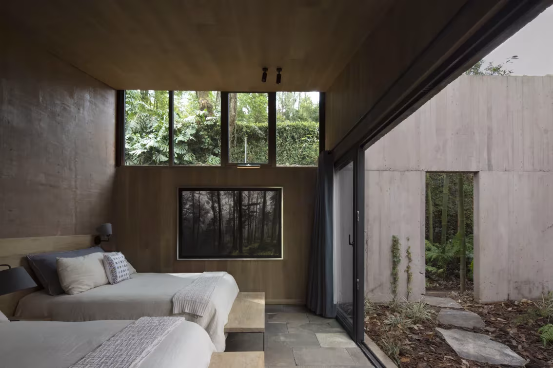 Dormitorio de la Casa L con camas, techo de madera y puerta corredera abierta al bosque