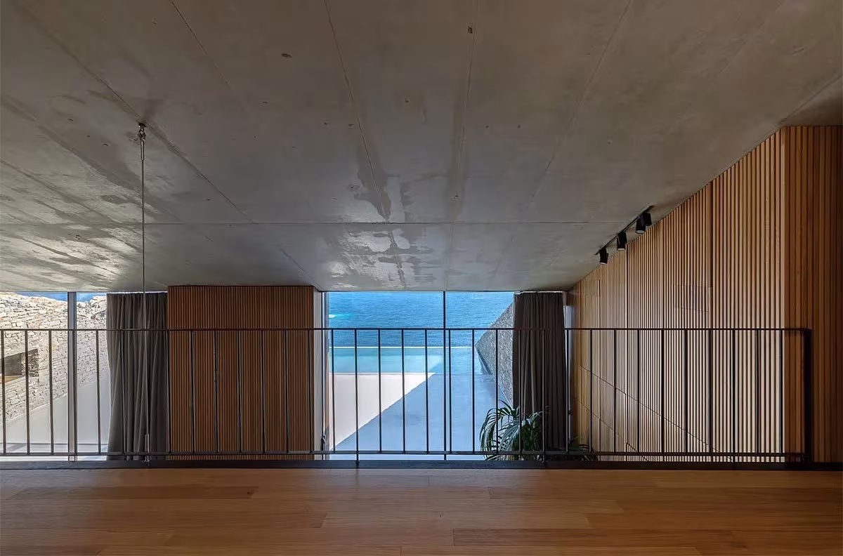 Altillo de la Casa NCaved con suelo de madera, barandilla metálica y ventana horizontal al mar Egeo