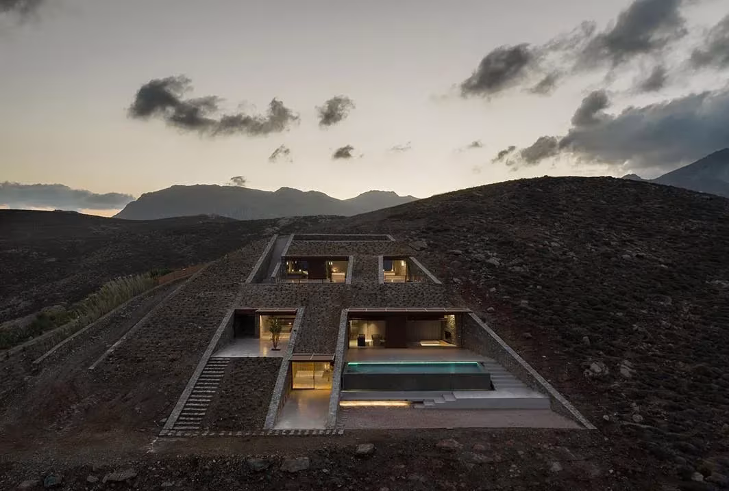 Casa NCaved de Mold Architects al anochecer, patios iluminados excavados en la ladera de Serifos