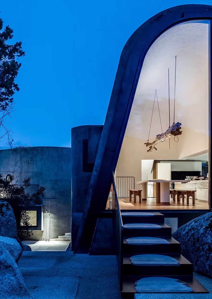 La Grintosa de Stefania Stera al anochecer, con un gran arco de hormigón que enmarca el interior iluminado y una escalera exterior