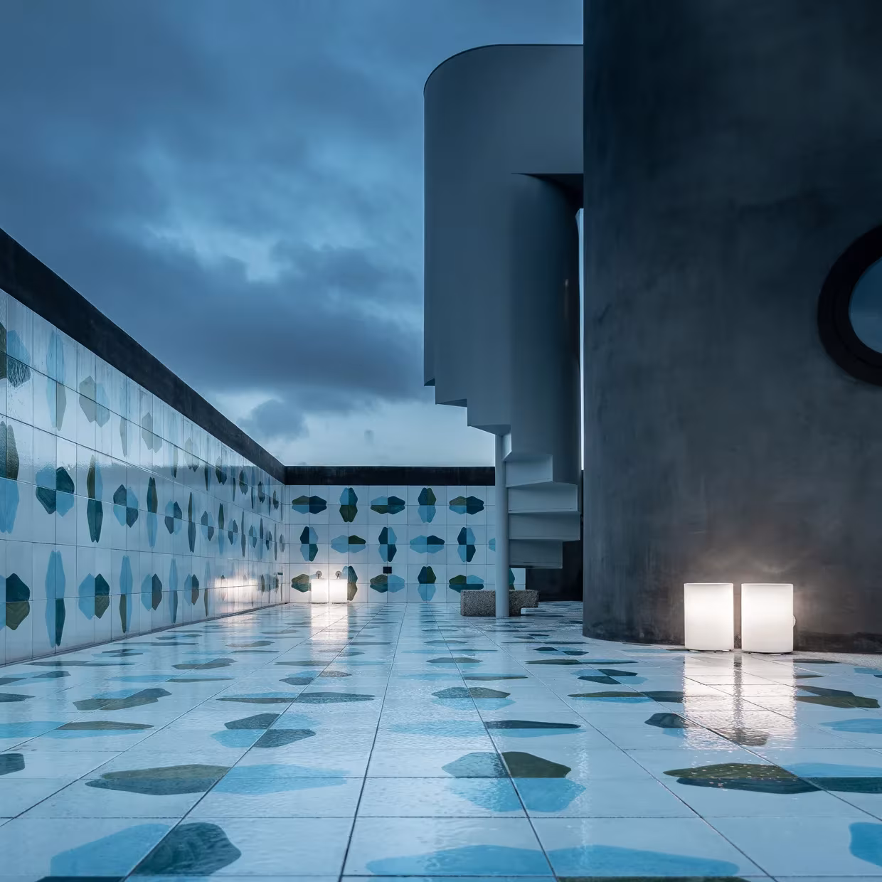 Terraza de La Grintosa al atardecer con suelo de baldosas de manchas azules, volúmenes cilíndricos y faroles cúbicos