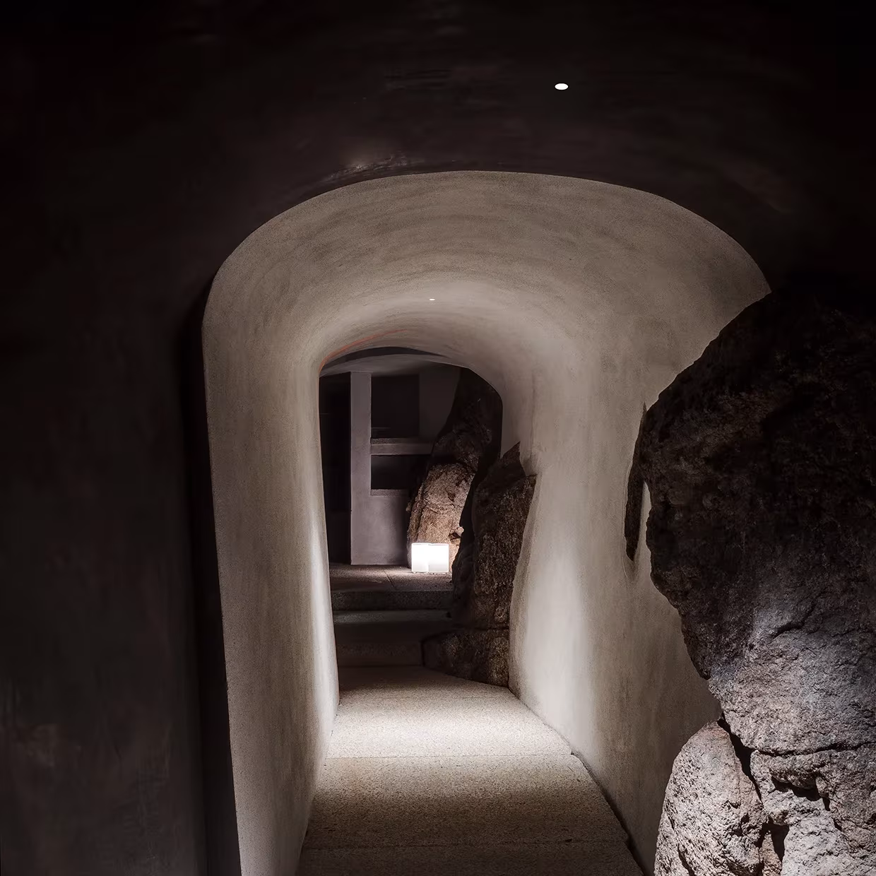 Pasadizo curvo de paredes blancas excavado entre las rocas en La Grintosa, iluminado con luz tenue