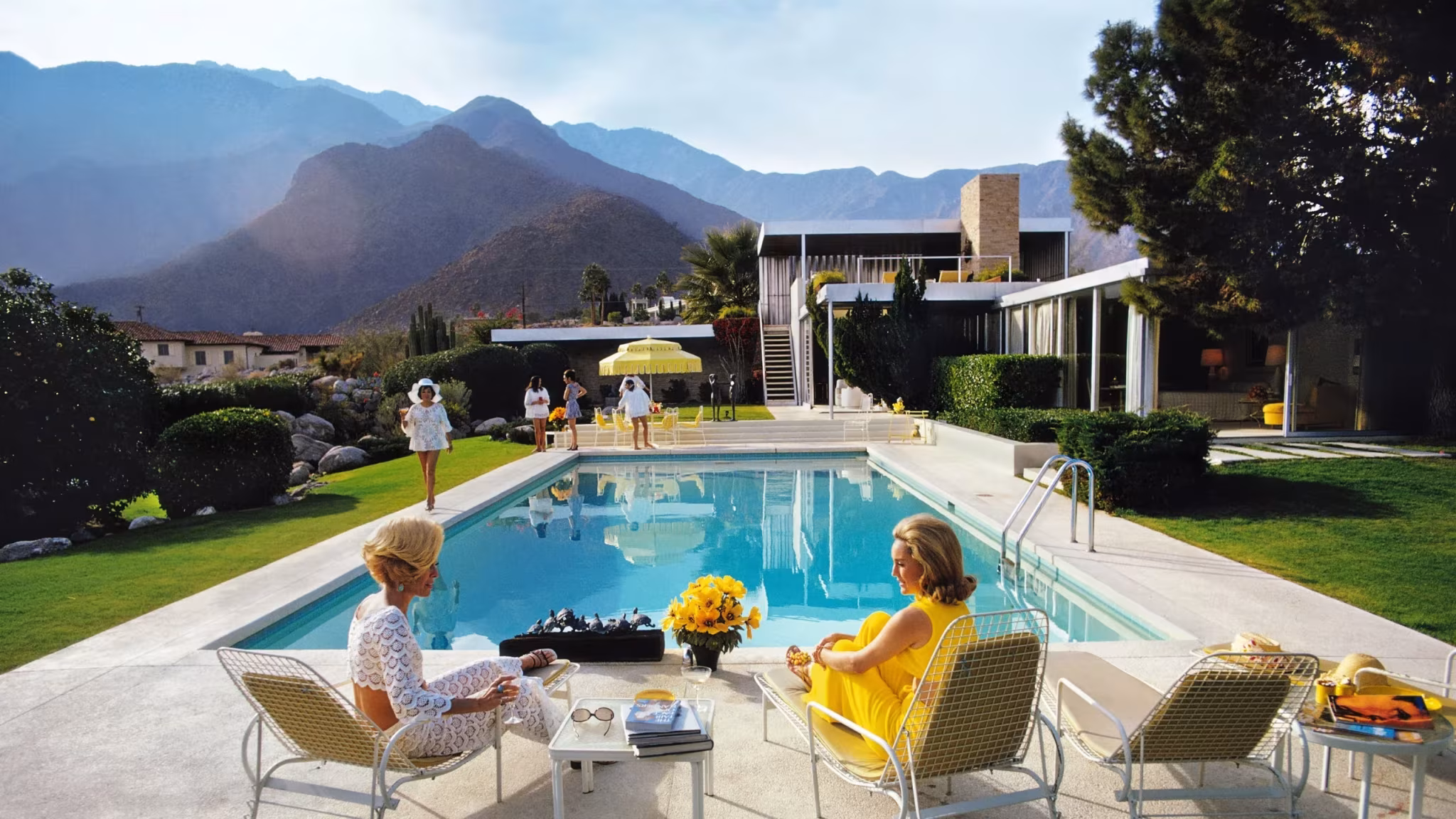 Kaufmann Desert House de Richard Neutra con su piscina, dos mujeres en tumbonas y montañas al fondo