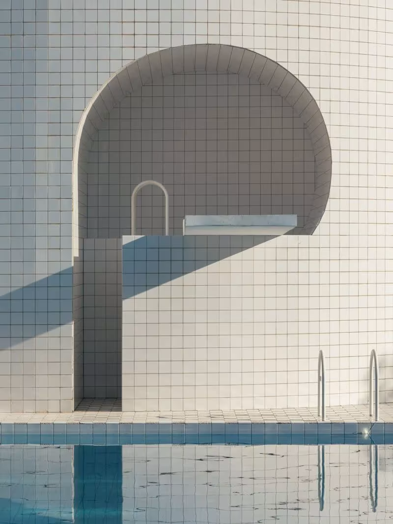 Piscina con muro de azulejo blanco y hornacina en arco, una piscina escondida de líneas geométricas