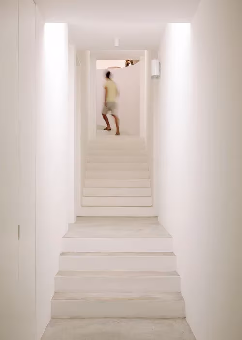 Escalera encalada entre muros blancos que baja con luz cenital en la Casa UM, Algarve