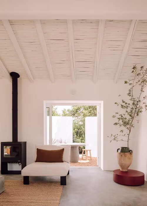Sala con estufa de leña, techo de cañizo y vigas blancas abierta a un patio en la Casa UM