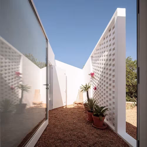 Patio estrecho entre celosías de ladrillo hueco encaladas con macetas de flores en la Casa UM