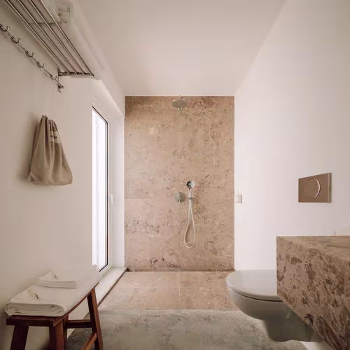 Baño con ducha revestida de piedra beige y encimera de mampostería en la Casa UM