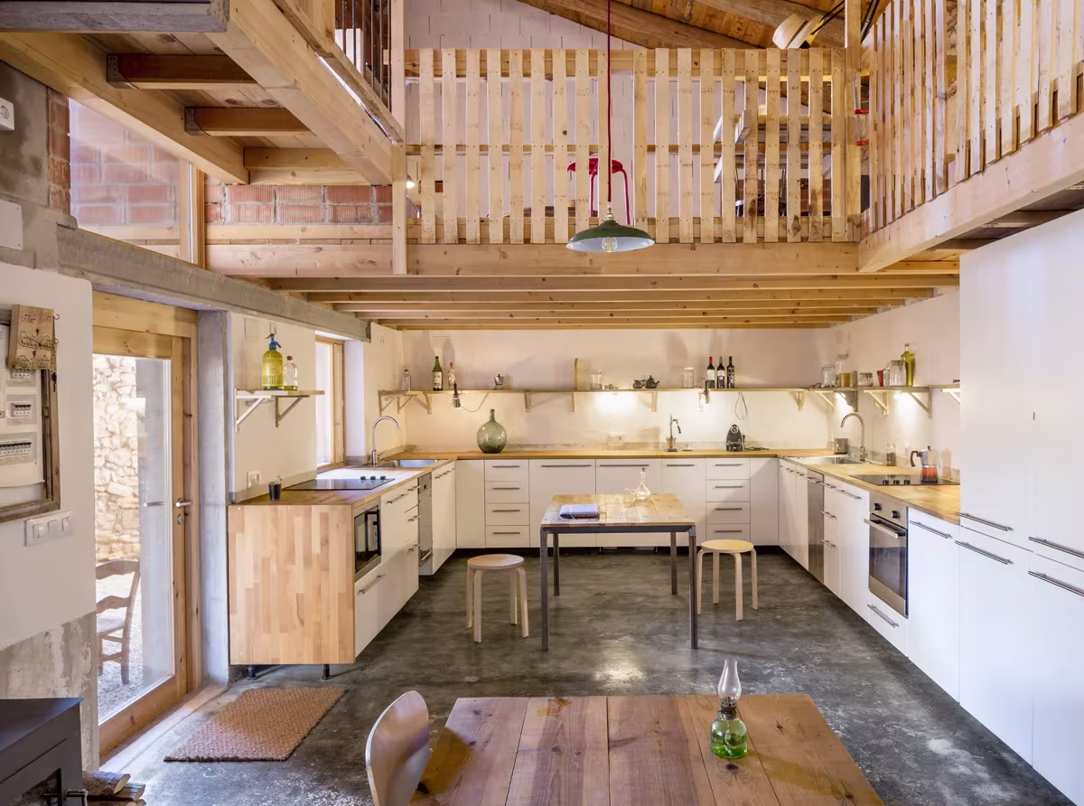 Cocina blanca y mesa de madera bajo un altillo con barandilla de listones en la Casa en Tres Primaveras