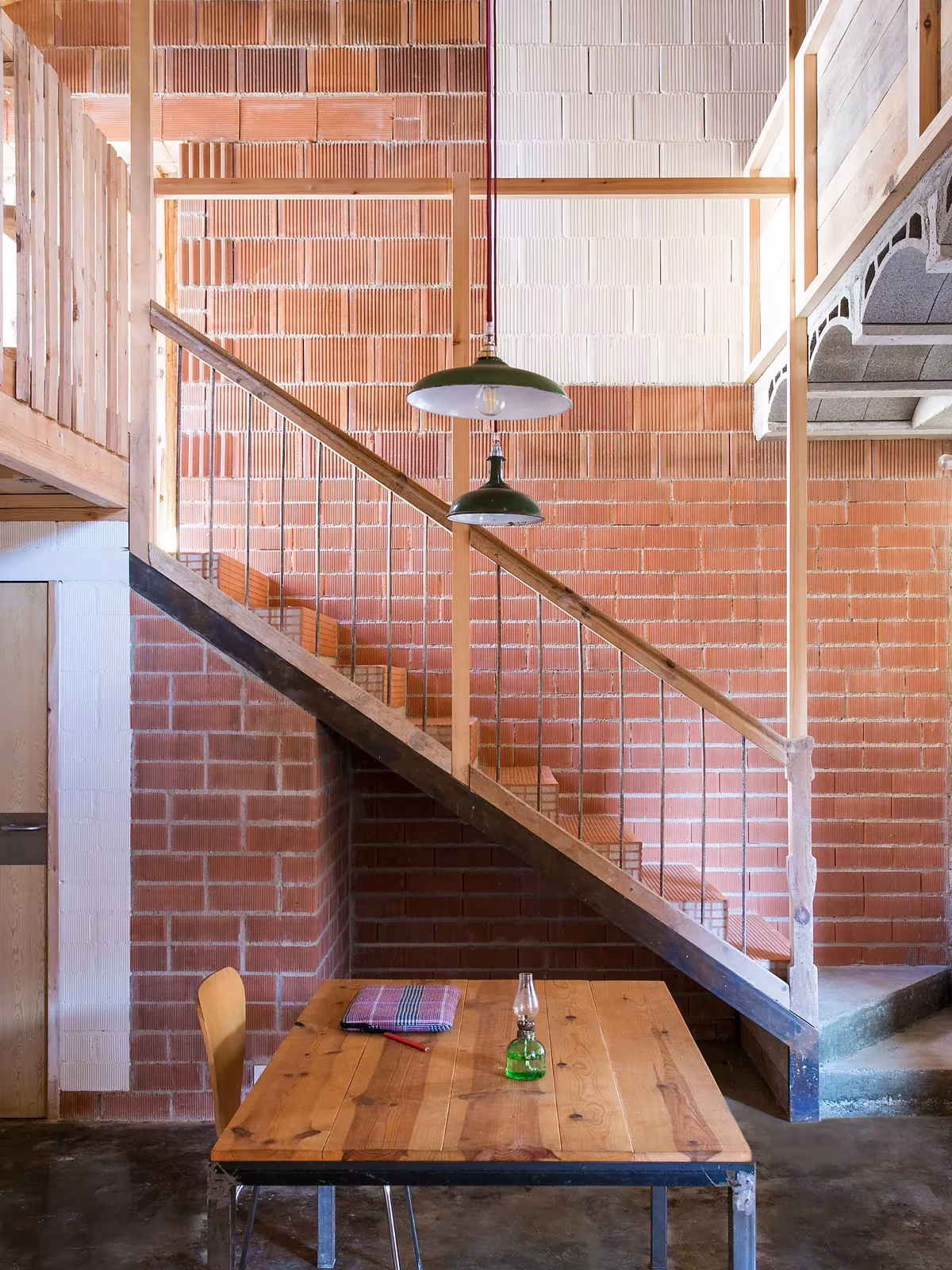 Escalera con barandilla metálica y comedor de madera junto al muro de ladrillo en Tres Primaveras