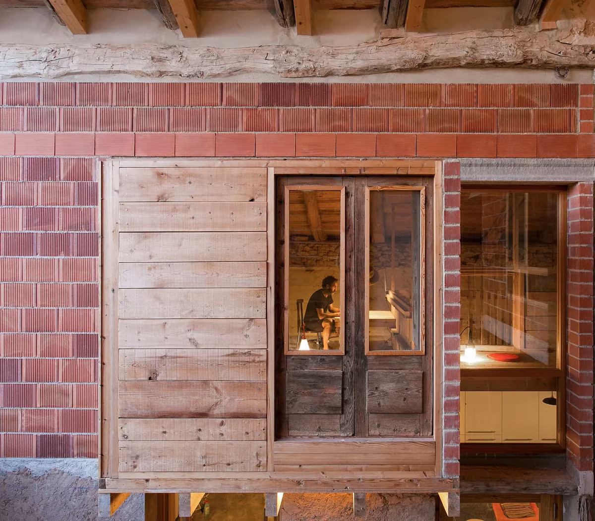Ventana con carpintería de madera reciclada y dintel de viga sobre el muro de ladrillo en Tres Primaveras
