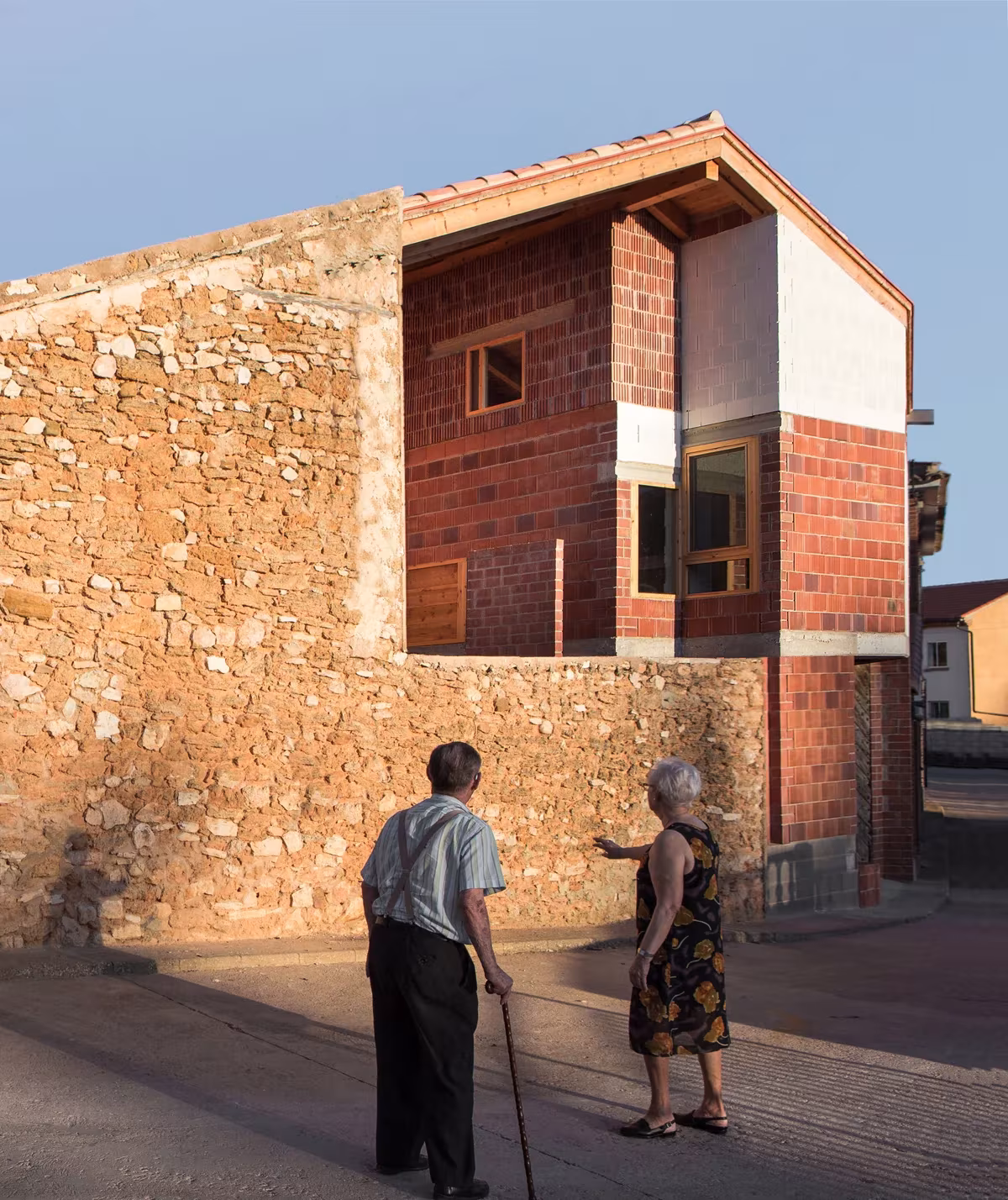 Casa en Tres Primaveras al atardecer, con muro de mampostería y dos vecinos paseando por la calle