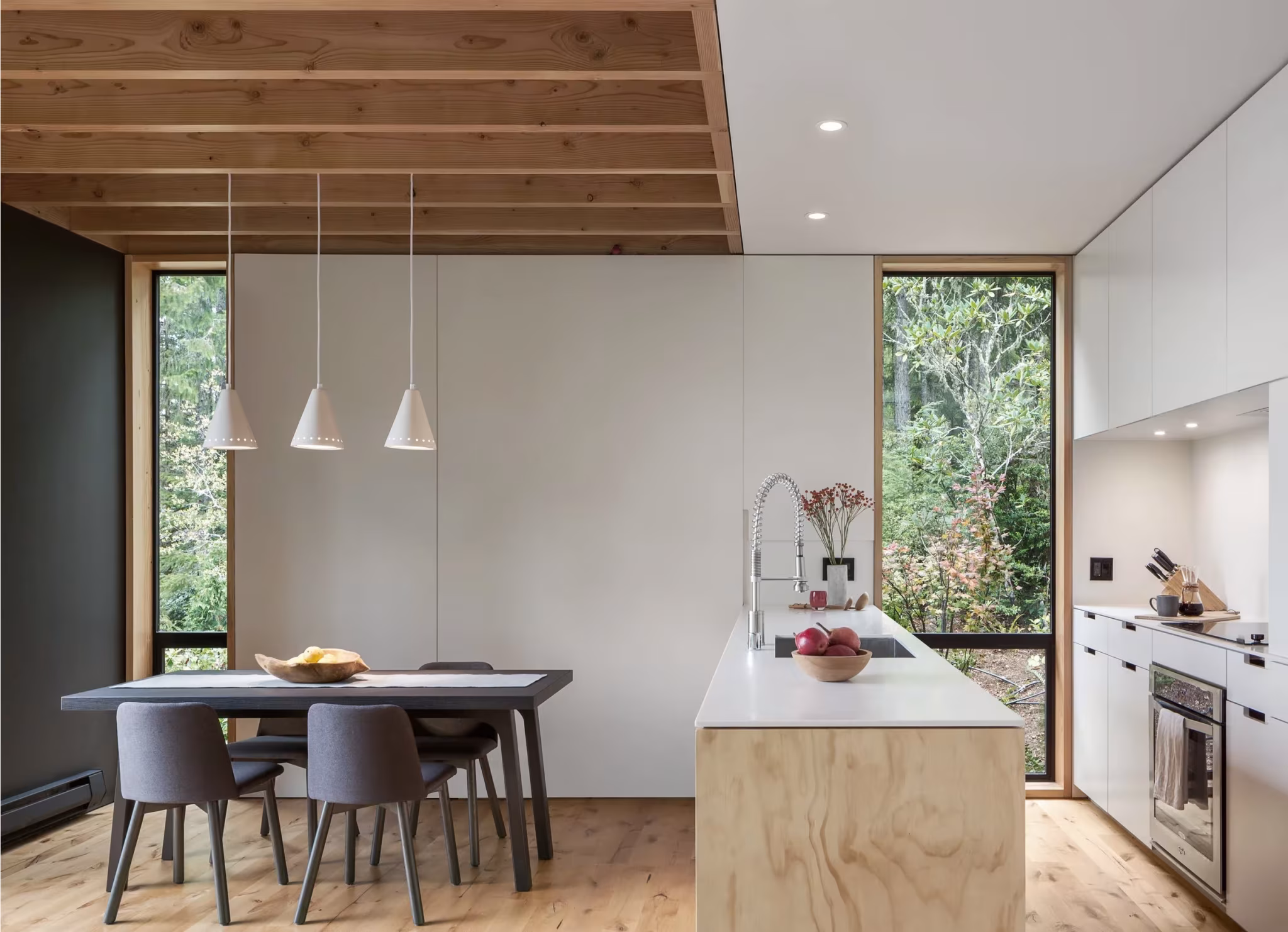Cocina con isla de madera contrachapada y comedor bajo vigas de madera vistas en Little House