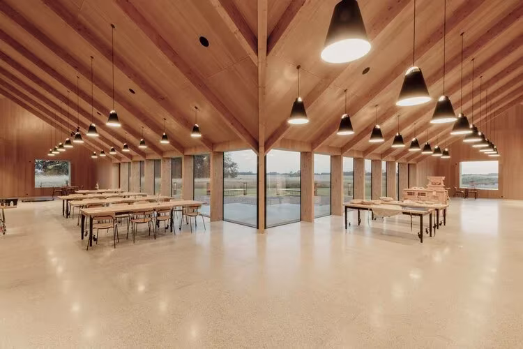 Sala del Kornets Hus con cubierta de madera, mesas largas y lámparas colgantes ante la cristalera