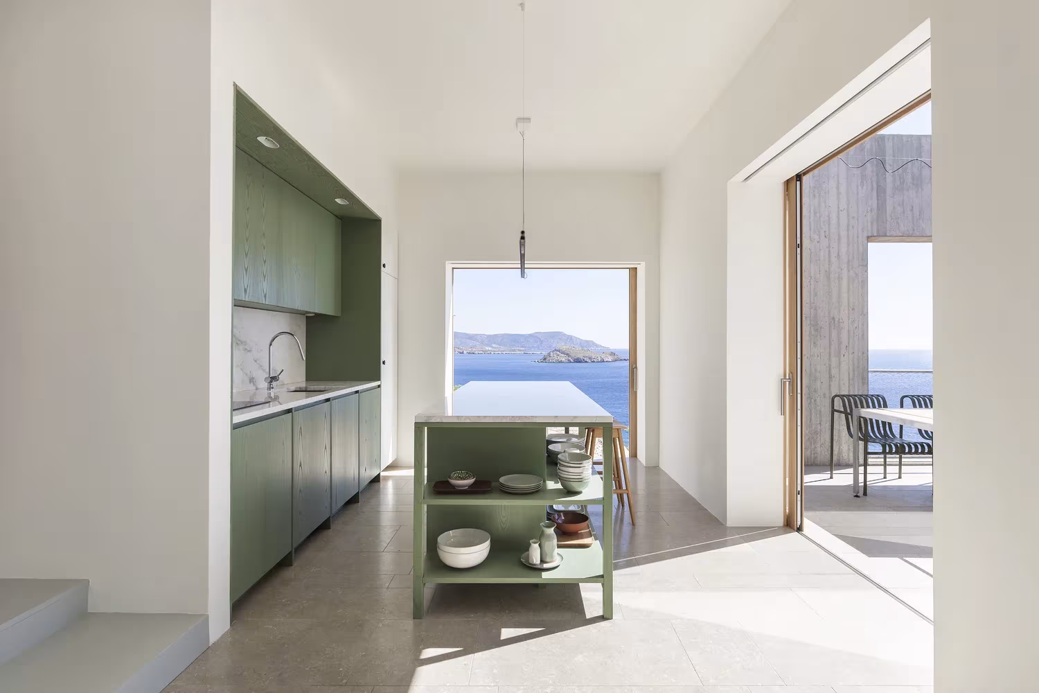 Cocina de armarios verdes con isla central y vistas al mar a través de un gran hueco en la Casa Patio