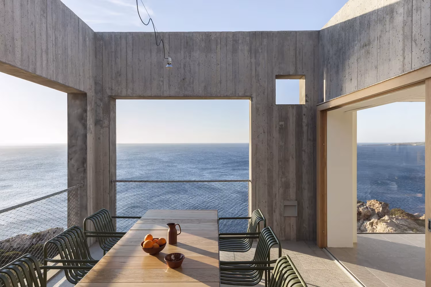 Comedor al aire libre de hormigón encofrado con tres grandes ventanales al mar en la Casa Patio
