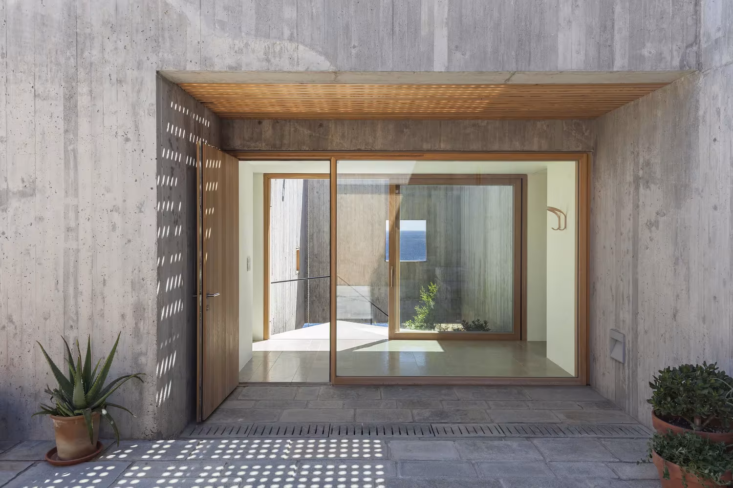 Porche de hormigón con techo de madera y puerta corredera que da al patio de la Casa Patio