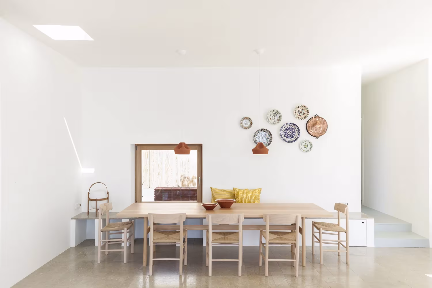 Comedor blanco con mesa de madera, sillas de madera clara y platos en la pared en la Casa Patio