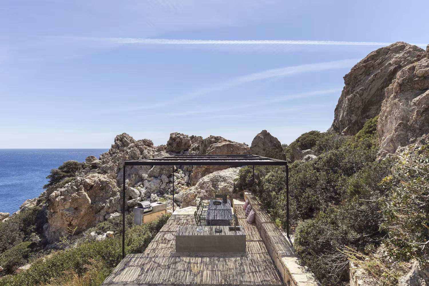Pérgola metálica con cañizo y zona de barbacoa sobre las rocas junto al mar, Casa Patio de OOAK