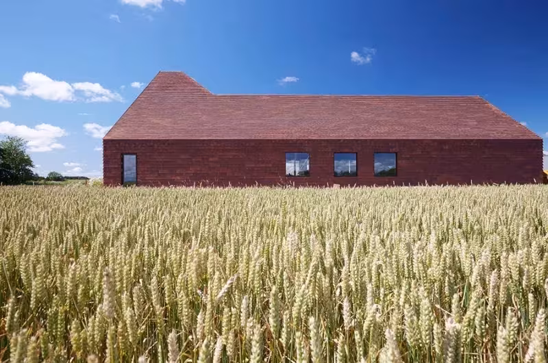 Fachada alargada de ladrillo rojo del Kornets Hus entre trigales, con ventanas apaisadas