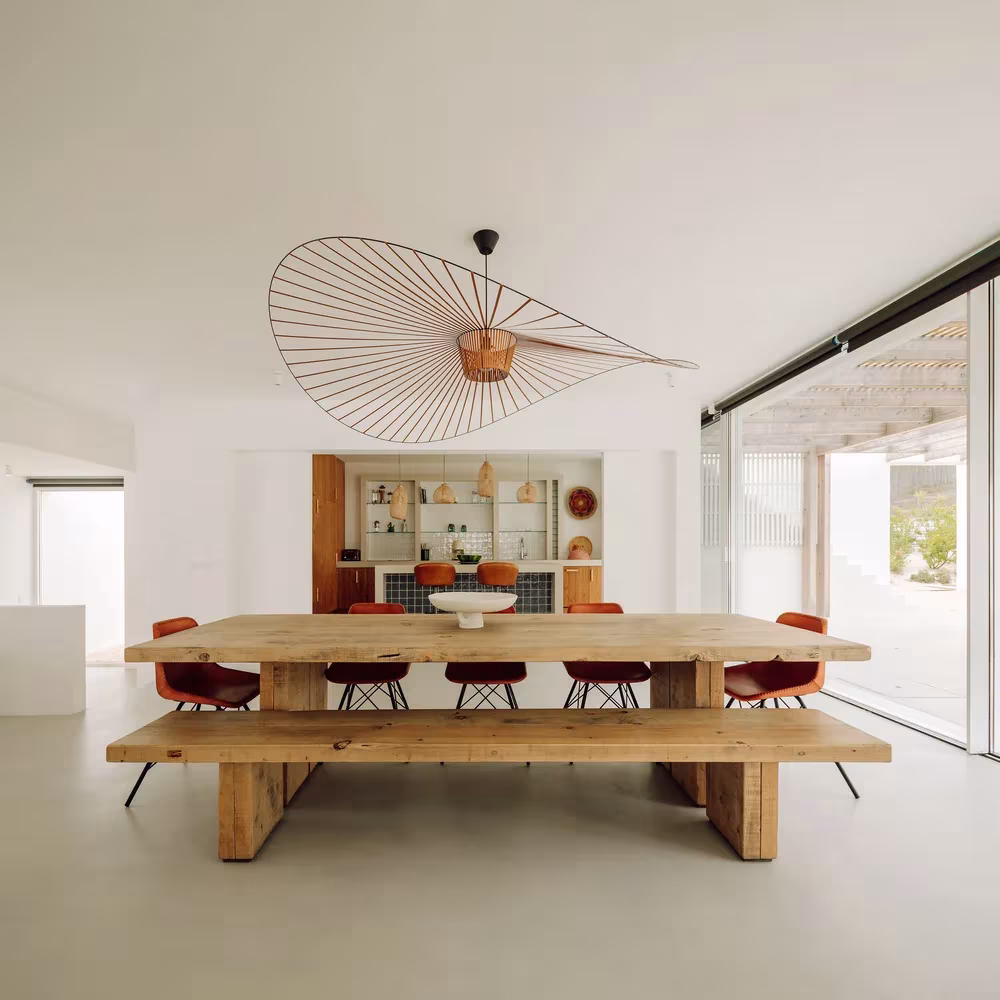 Mesa de madera con banco y sillas rojas bajo una gran lámpara de varillas en Comporta 10, Alentejo