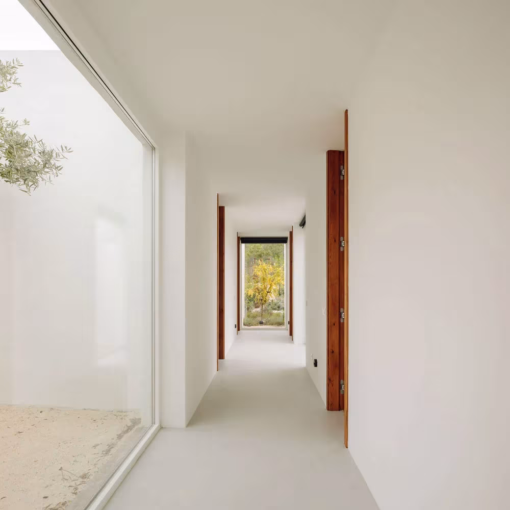 Pasillo blanco de Comporta 10 junto a un ventanal sobre un patio de arena, con puertas de madera