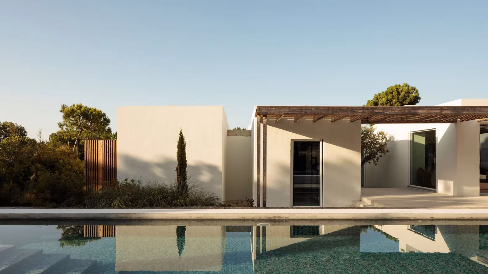 Piscina de Comporta 10 reflejando la pérgola de madera, los muros blancos y los pinos del Alentejo