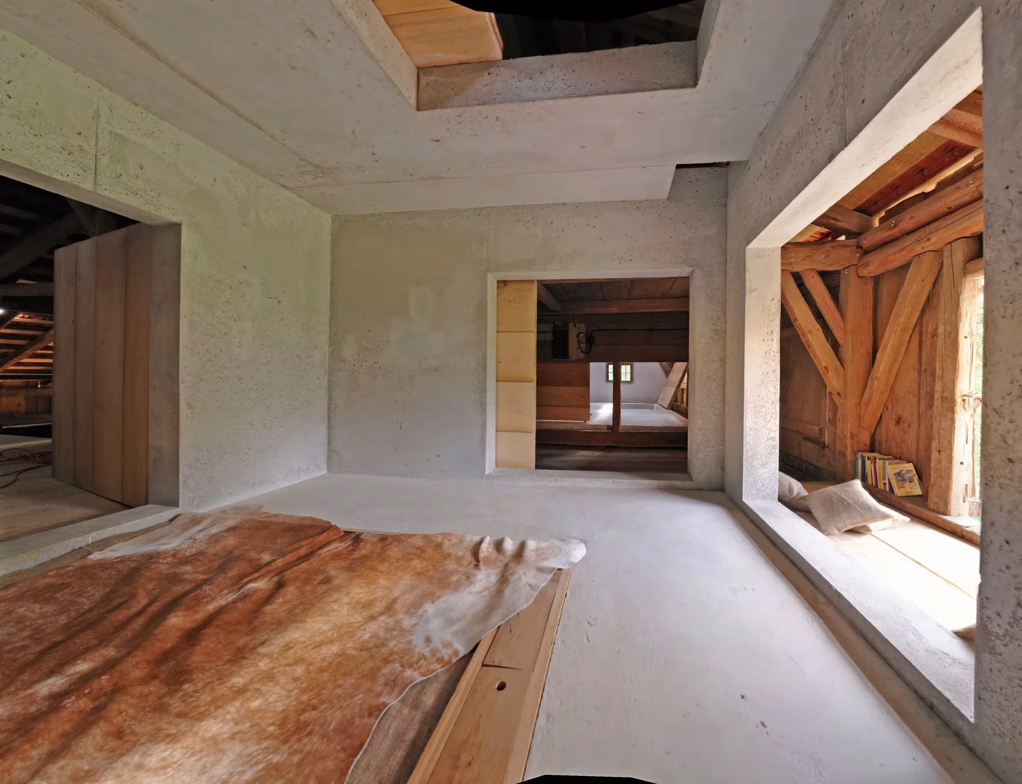 Estancia con muros de hormigón claro y una gran ventana que recorta el entramado de madera original
