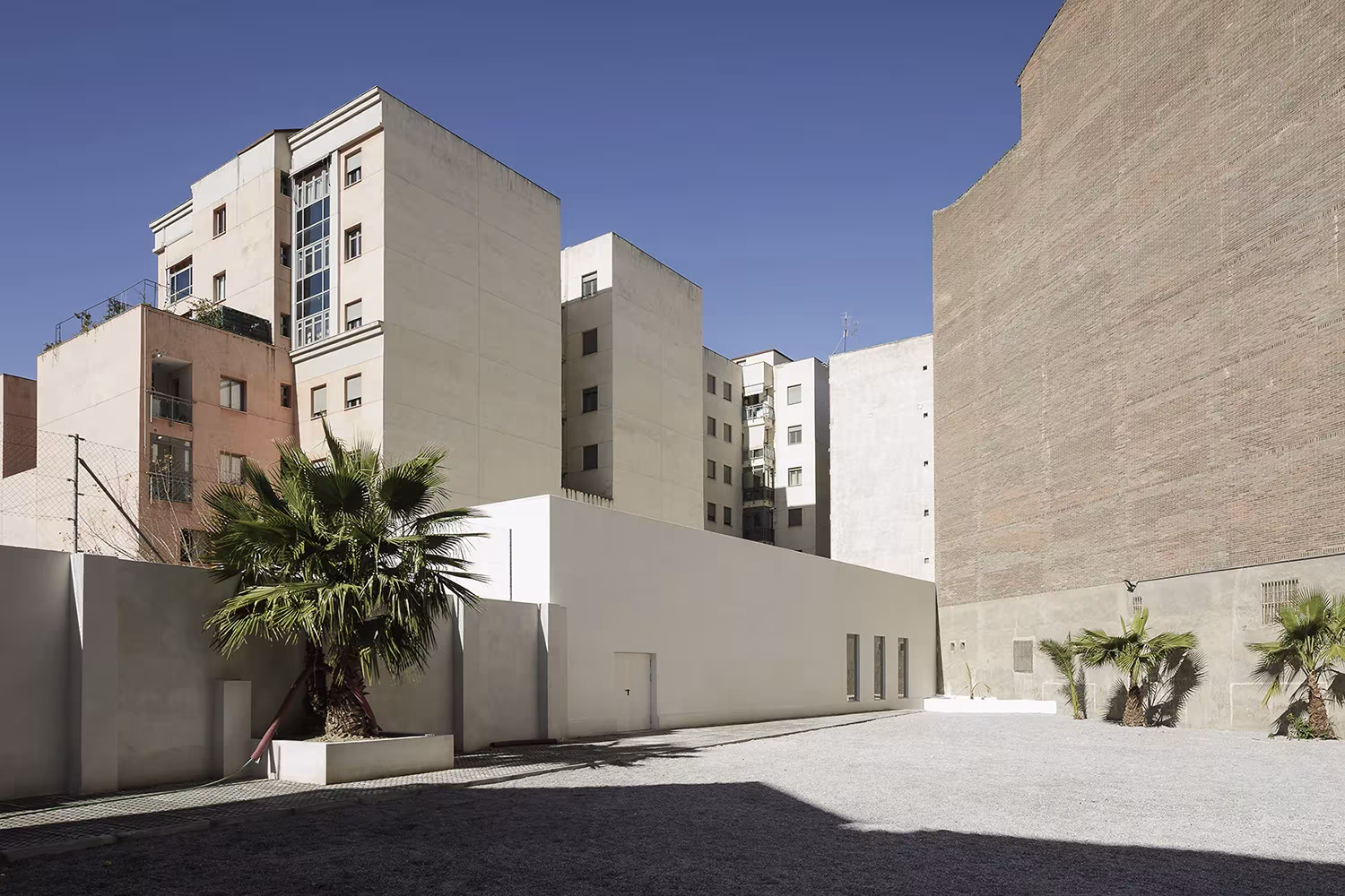 Exterior del polideportivo de Elisa Valero en Granada, volumen blanco entre edificios de viviendas y palmeras