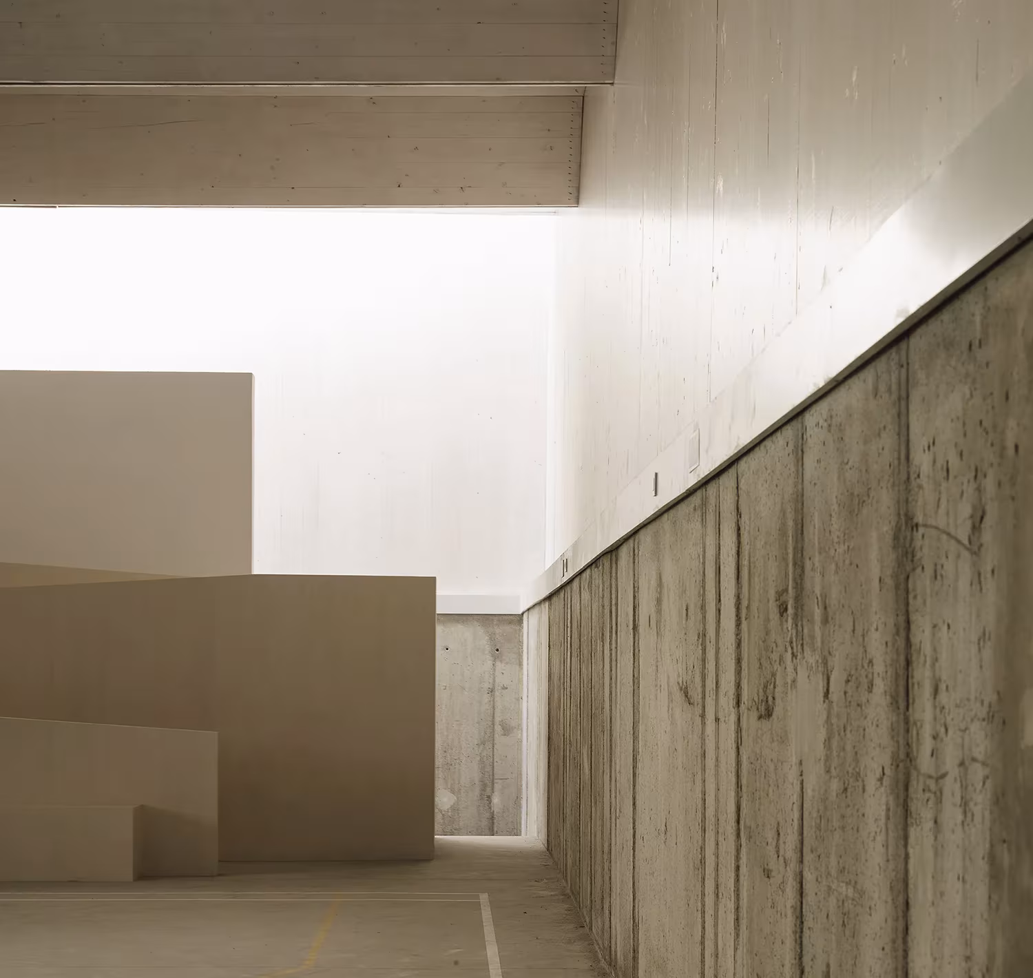 Muro de hormigón encofrado y planos blancos iluminados desde arriba en el polideportivo de Granada