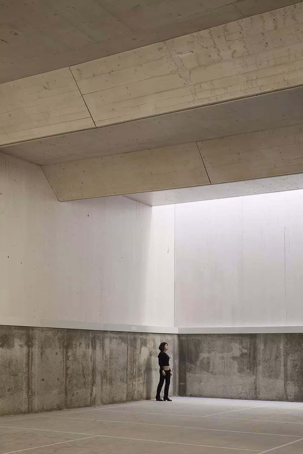 Persona pequeña junto al muro de hormigón bajo un gran lucernario en el polideportivo de Elisa Valero