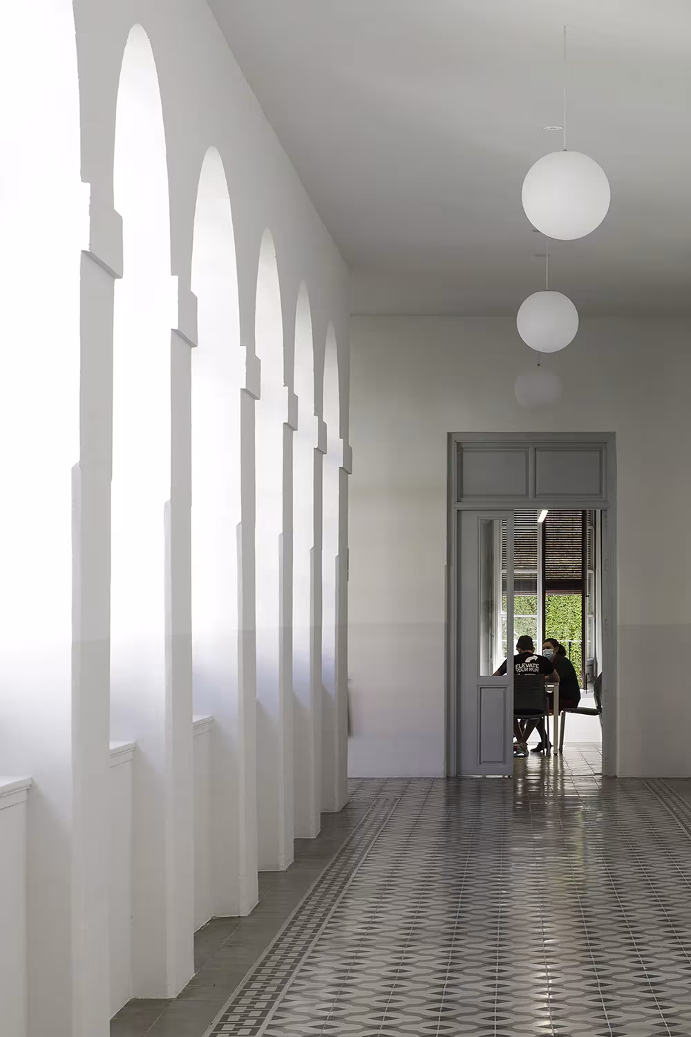 Galería de arcos blancos con lámparas de globo y suelo hidráulico en el antiguo convento rehabilitado de Granada