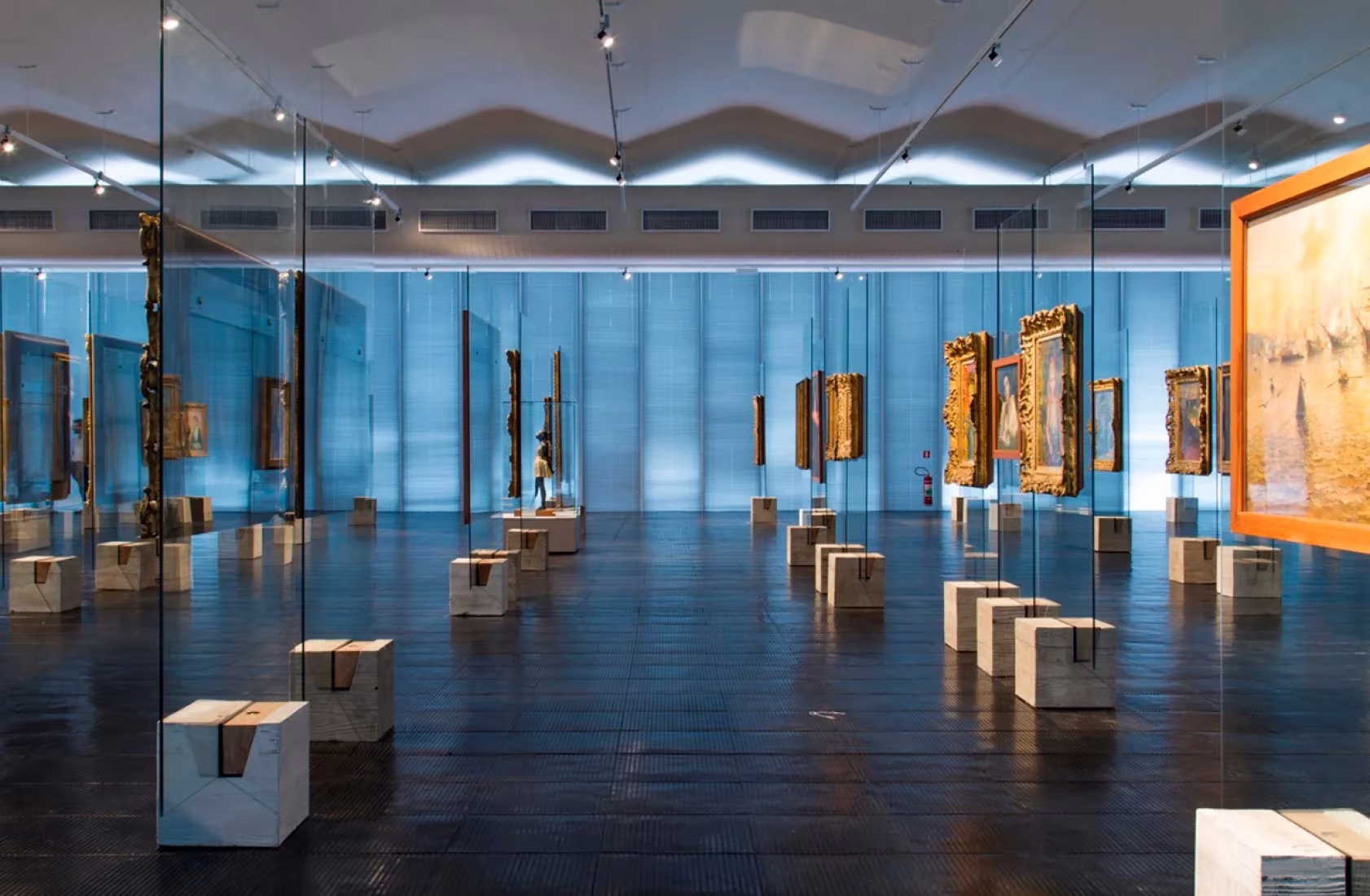 Sala de exposiciones del MASP con caballetes de vidrio y peanas de madera bajo techo ondulado
