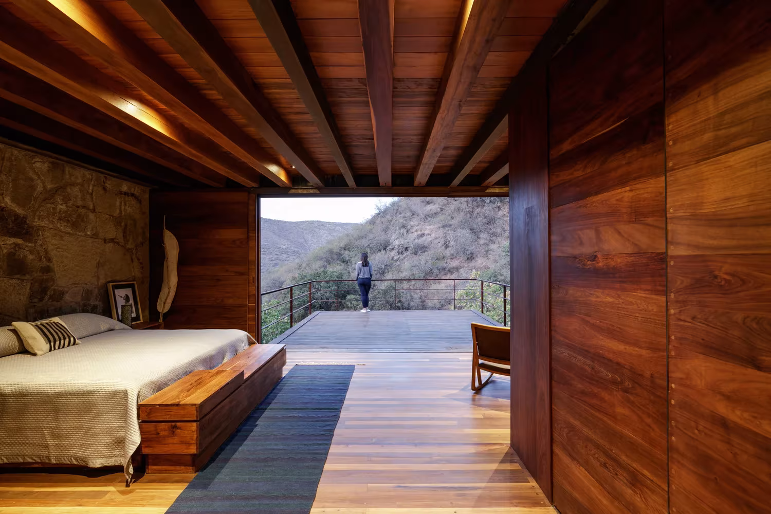 Dormitorio con cama de madera y terraza abierta a las colinas en la Cabaña Teitipac