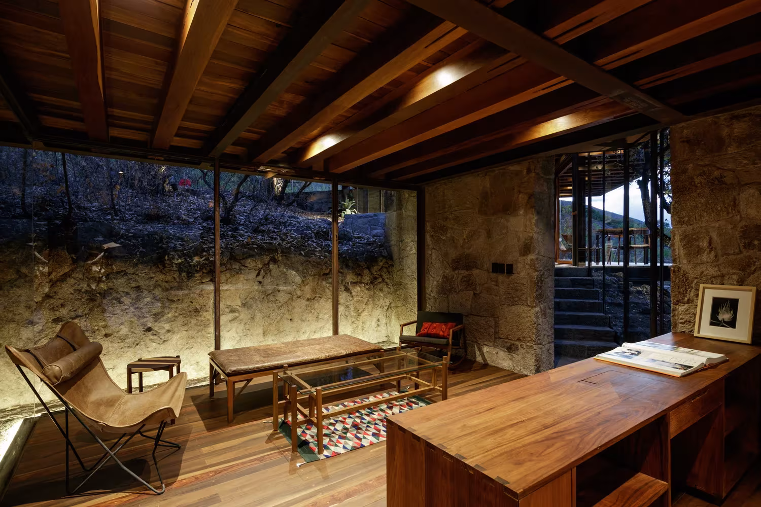 Sala de estar de la Cabaña Teitipac con butaca de cuero, escritorio de madera y muros de piedra