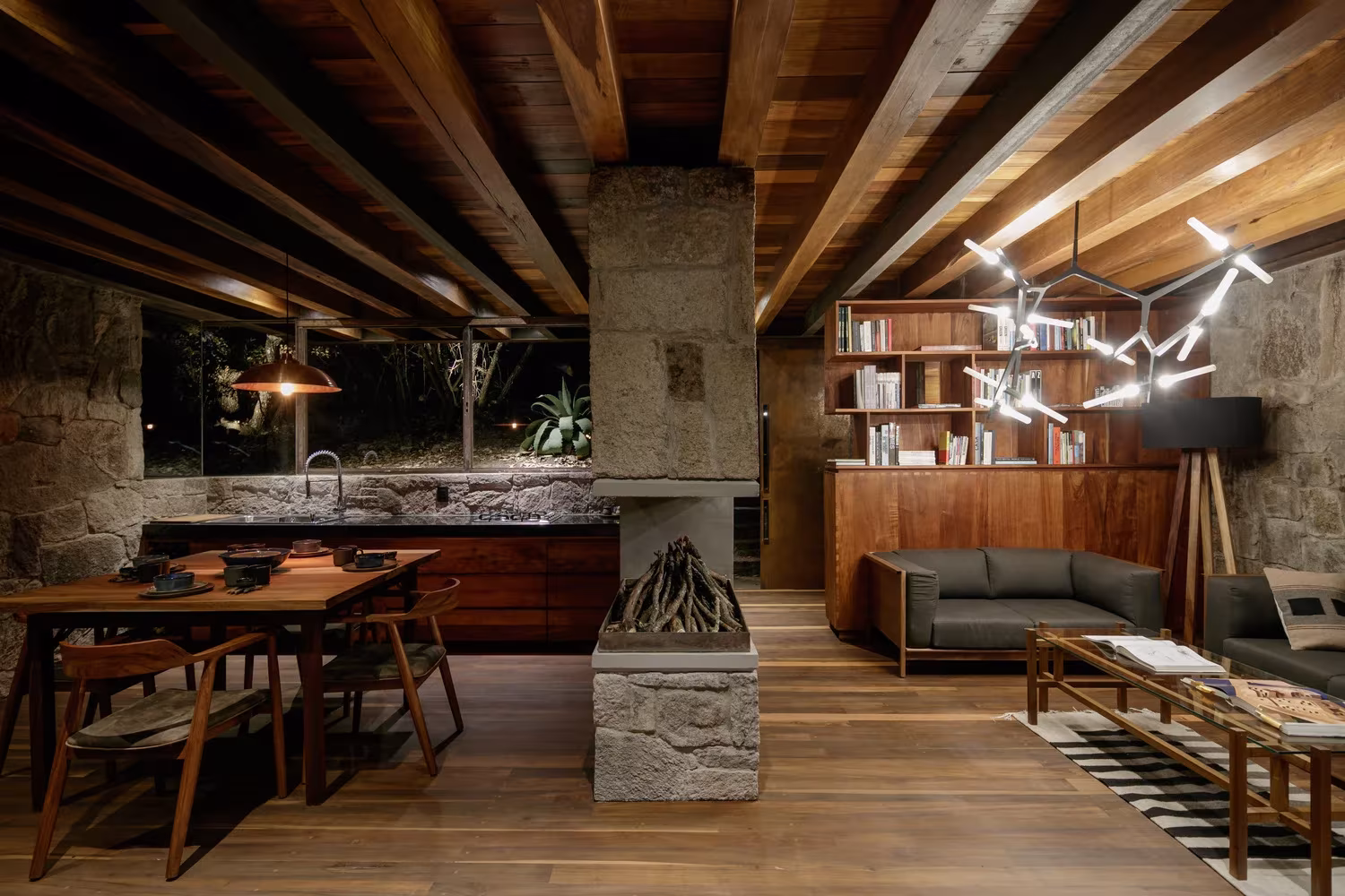 Cocina y comedor de la Cabaña Teitipac con chimenea de piedra central y techo de vigas de madera