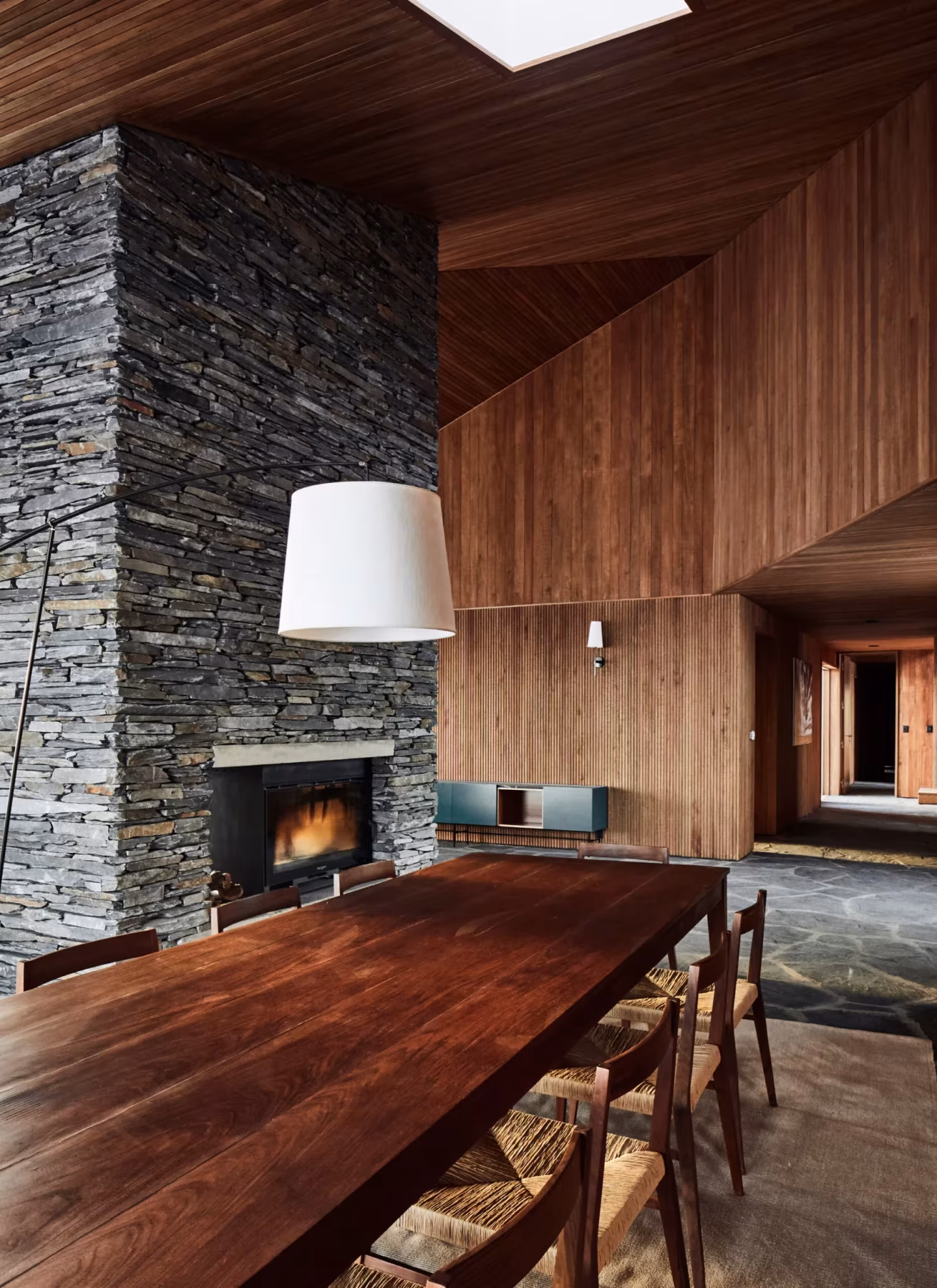 Comedor con chimenea de pizarra apilada y paramentos de madera a doble altura en Morro Chico