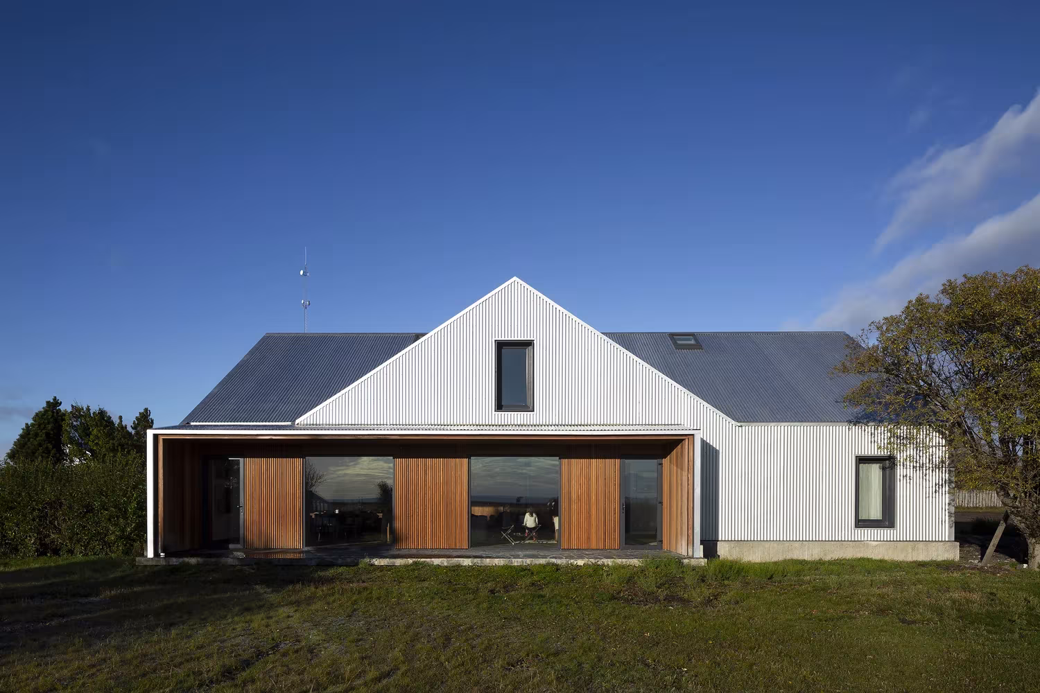Casa de revestimiento blanco y contraventanas de madera bajo un cielo azul en Morro Chico, de RDR Architectes
