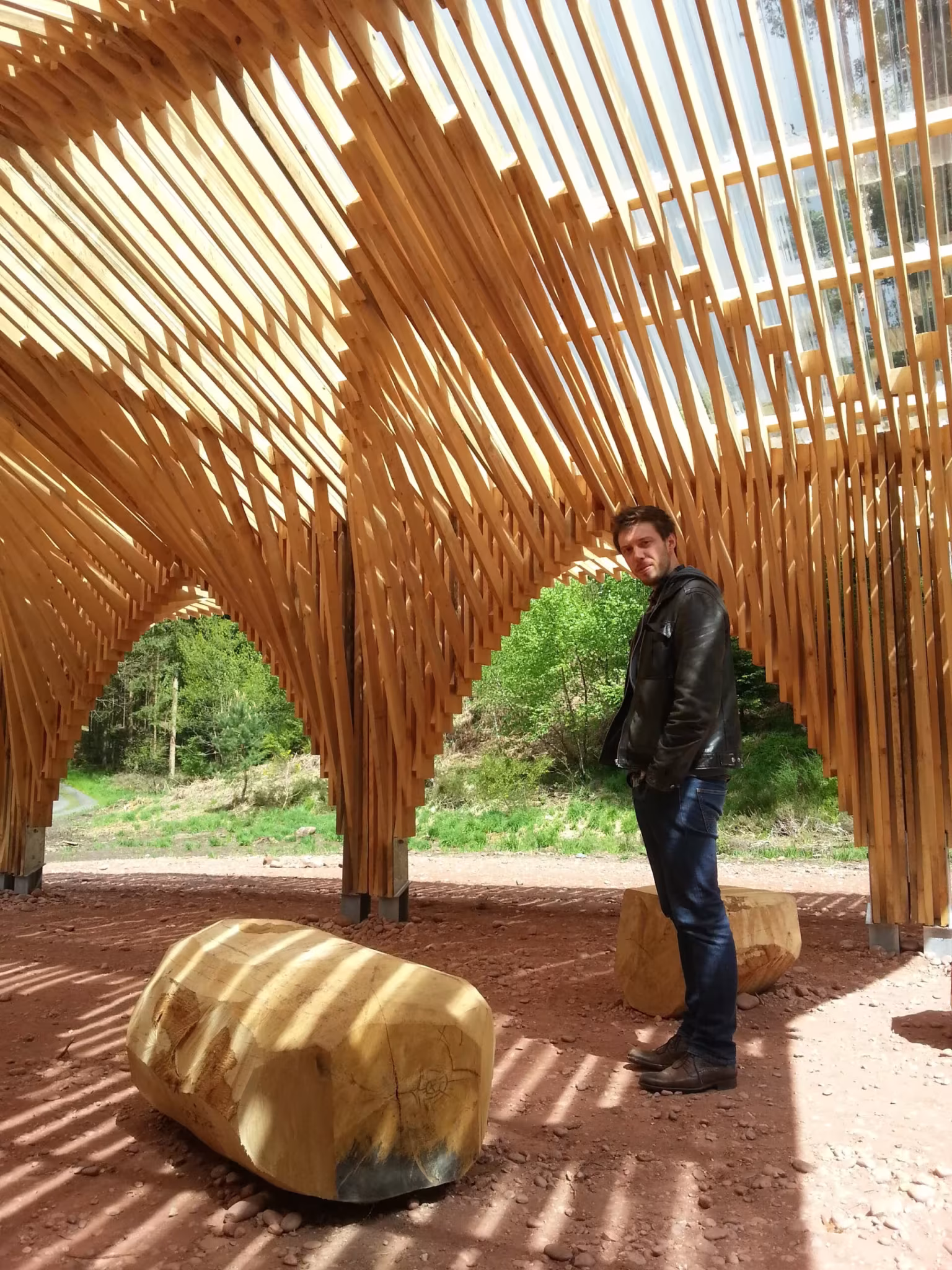 Visitante junto a un asiento de tronco bajo los arcos de pino del pabellón de Bertrichamps