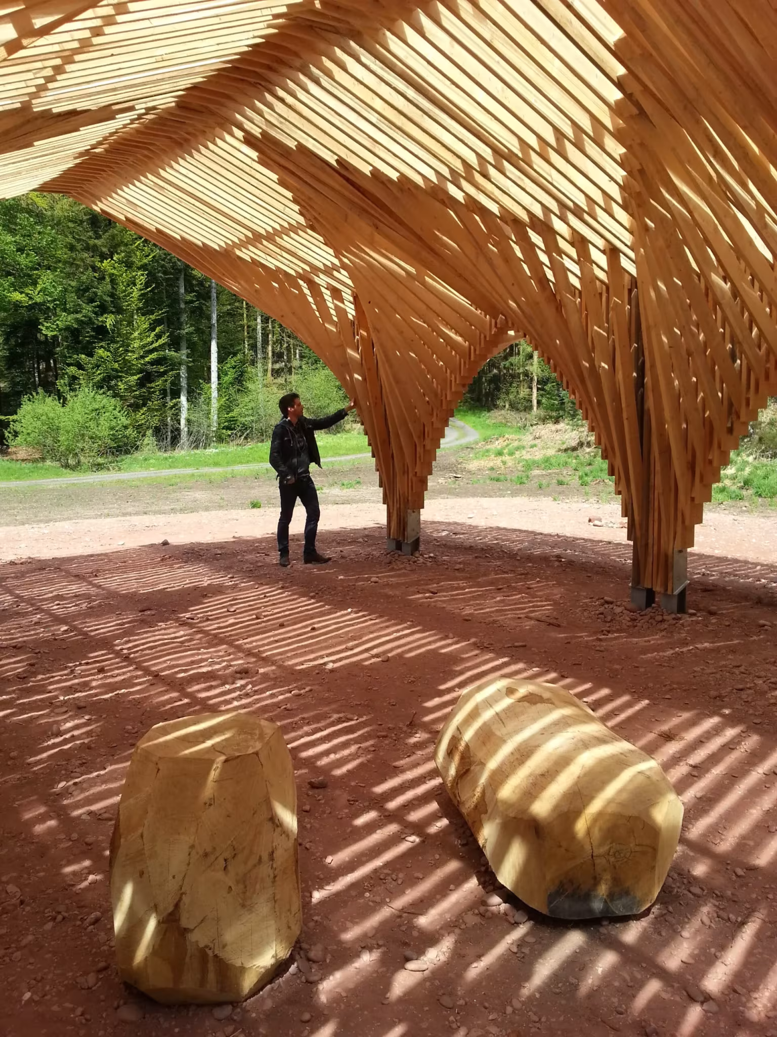 Sombras de los listones sobre el suelo rojizo y bloques de madera bajo la arquería de Bertrichamps