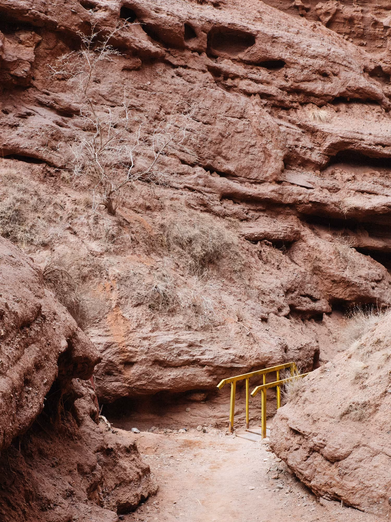 Paso estrecho entre rocas rojas erosionadas con una baranda amarilla, fotografía de Yuri Andries