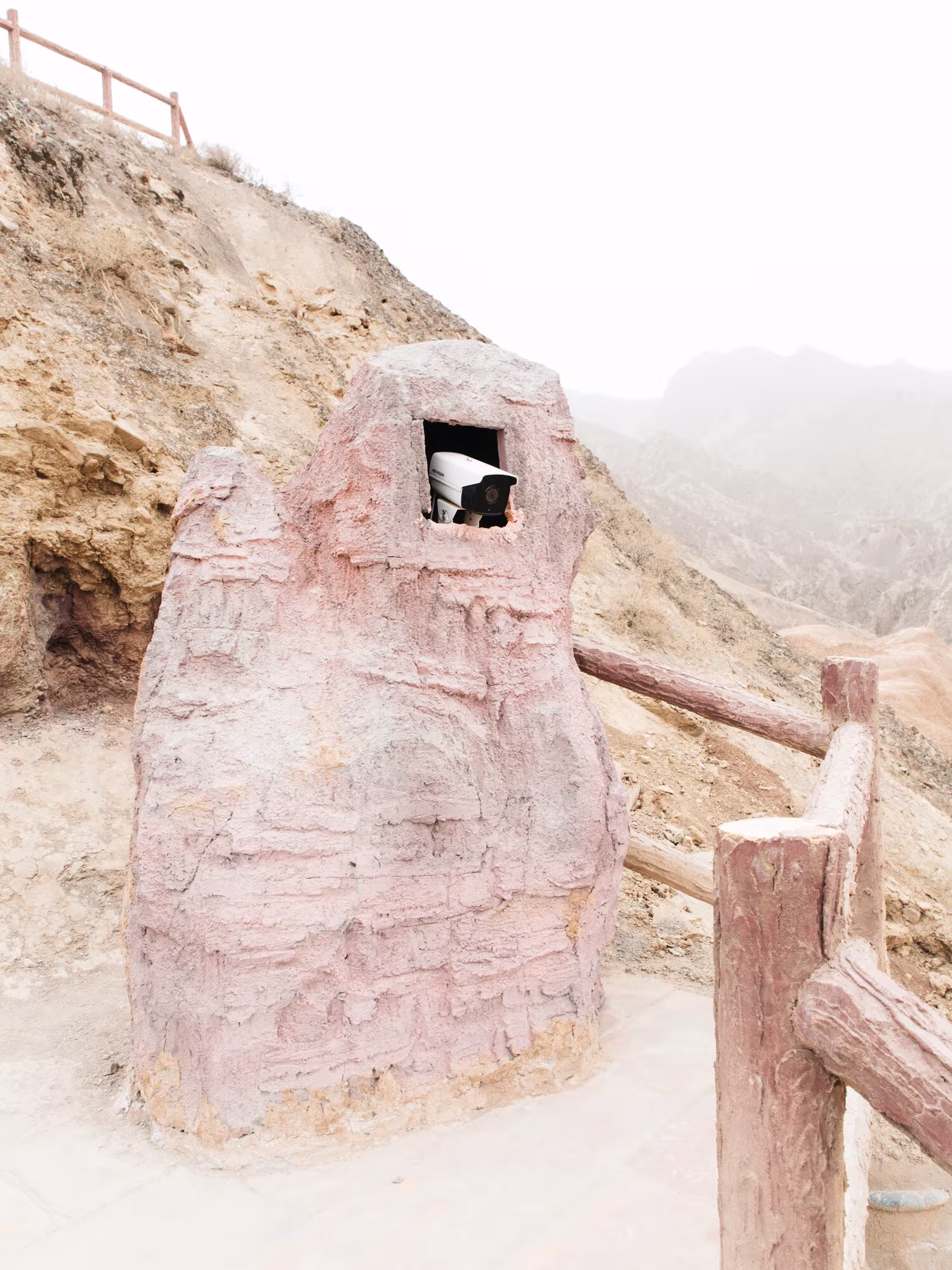 Escultura rosada de piedra artificial con un hueco en lo alto junto a una valla de madera, en la Nueva Ruta de la Seda