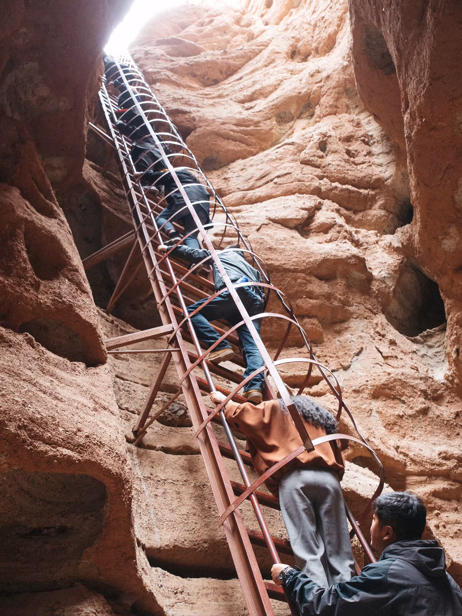 Visitantes subiendo por una escalera metálica entre paredes de roca roja en la Nueva Ruta de la Seda