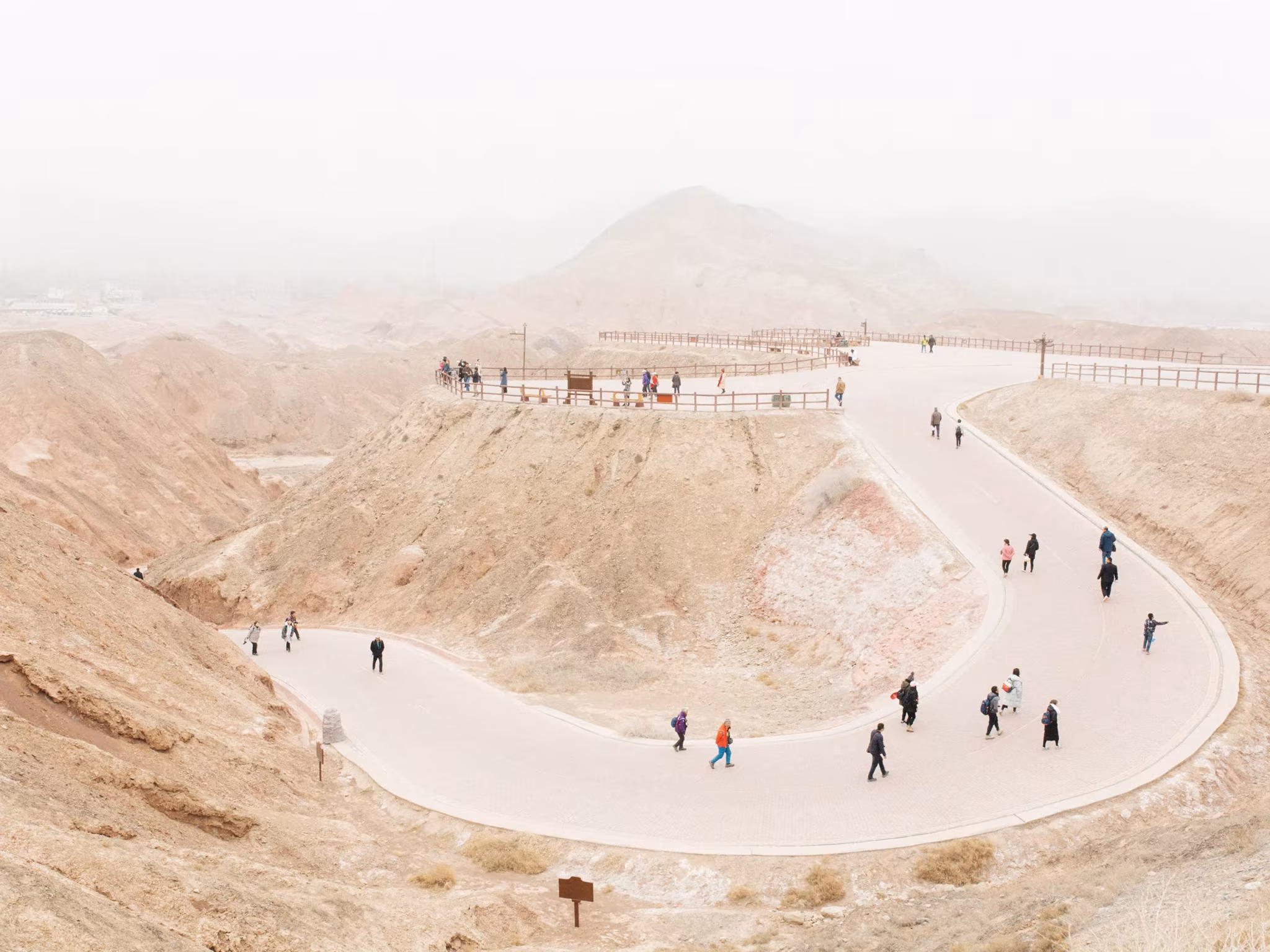 Sendero en curva con grupos de visitantes sobre un mirador en un paisaje de erosión y neblina